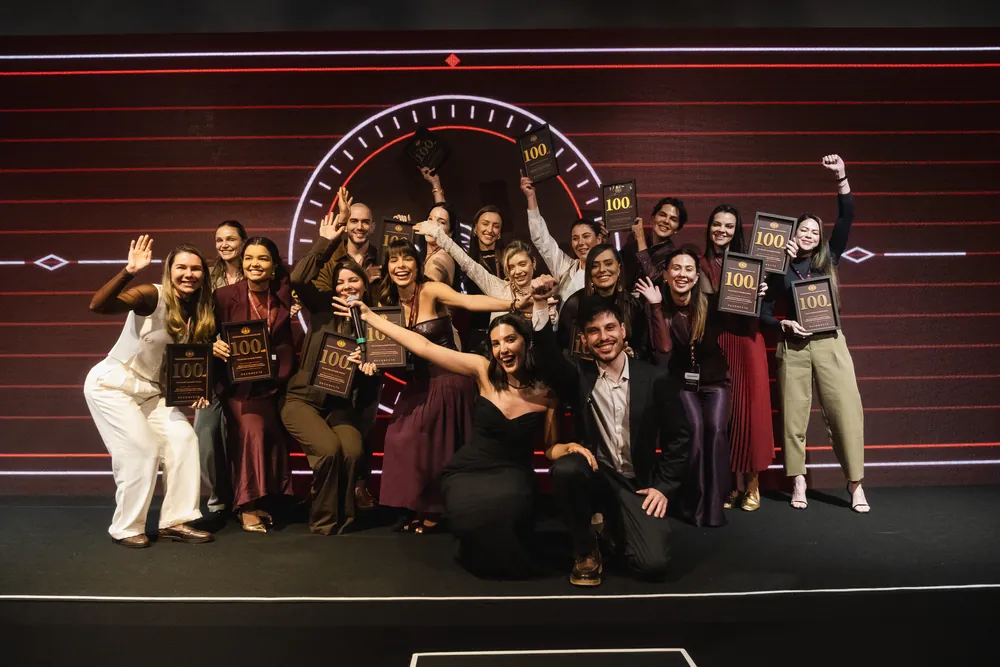 Grupo de doutoras premiadas vibrando no palco com as placas de 100 mil