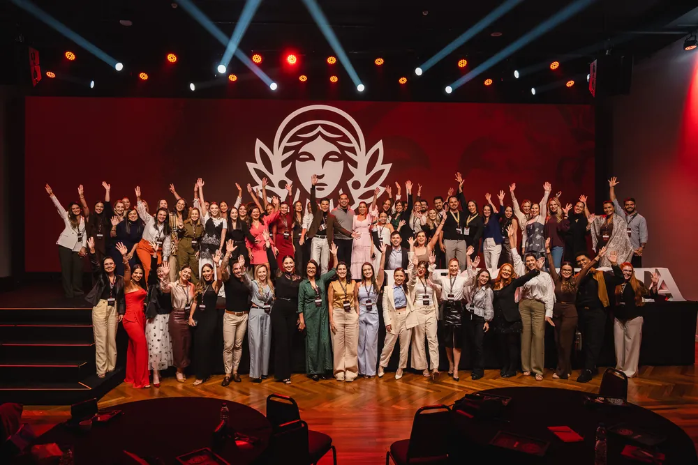 Dezenas de pessoas de braços erguidos no palco do evento, diante do emblema da Reconecta no telão